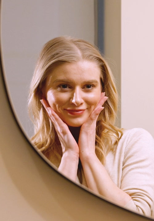 Woman looking in mirror with hands on cheeks