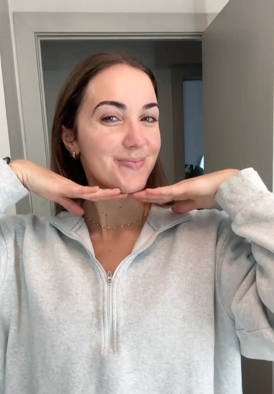 Woman posing with hands under face in a neutral indoor setting
