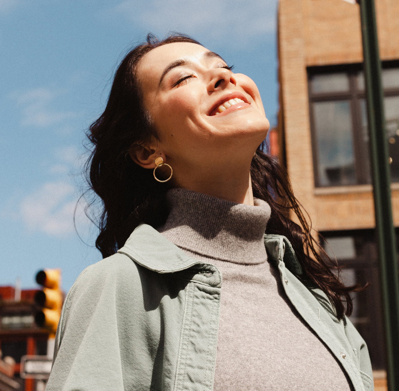 woman walking in city and looking up at sunny sky